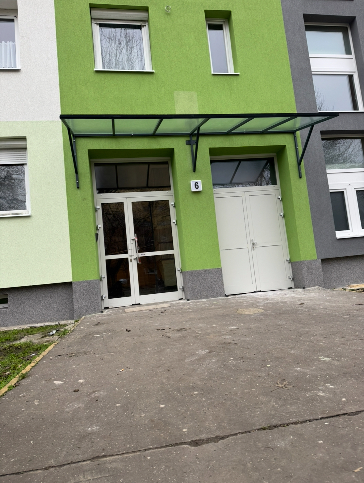 Referenciák – erkélyfelújítás és üvegezés Egyedi gyártású előtető szerkezet készült statikailag méretezett acélvázzal, az épület adottságaihoz igazítva. A fedést drótüveg biztosítja, amely tartós, időjárásálló megoldást nyújt, miközben megőrzi a bejárat világosságát.